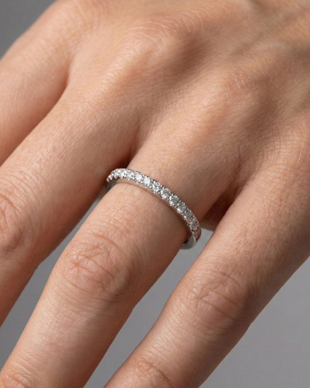 A top-down view of a 14K white gold thin band ring with a continuous line of petite, pavé-set round jewels on a finger of a hand.